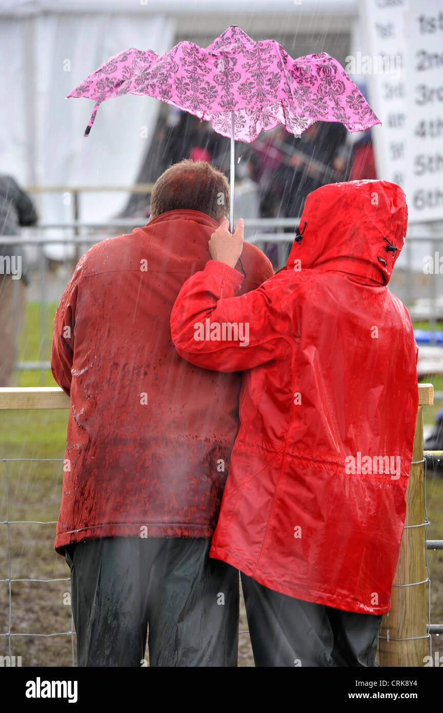 Par refugiarse bajo un pequeño paraguas en una tormenta en el Royal Highland Show, Edimburgo. Foto de stock