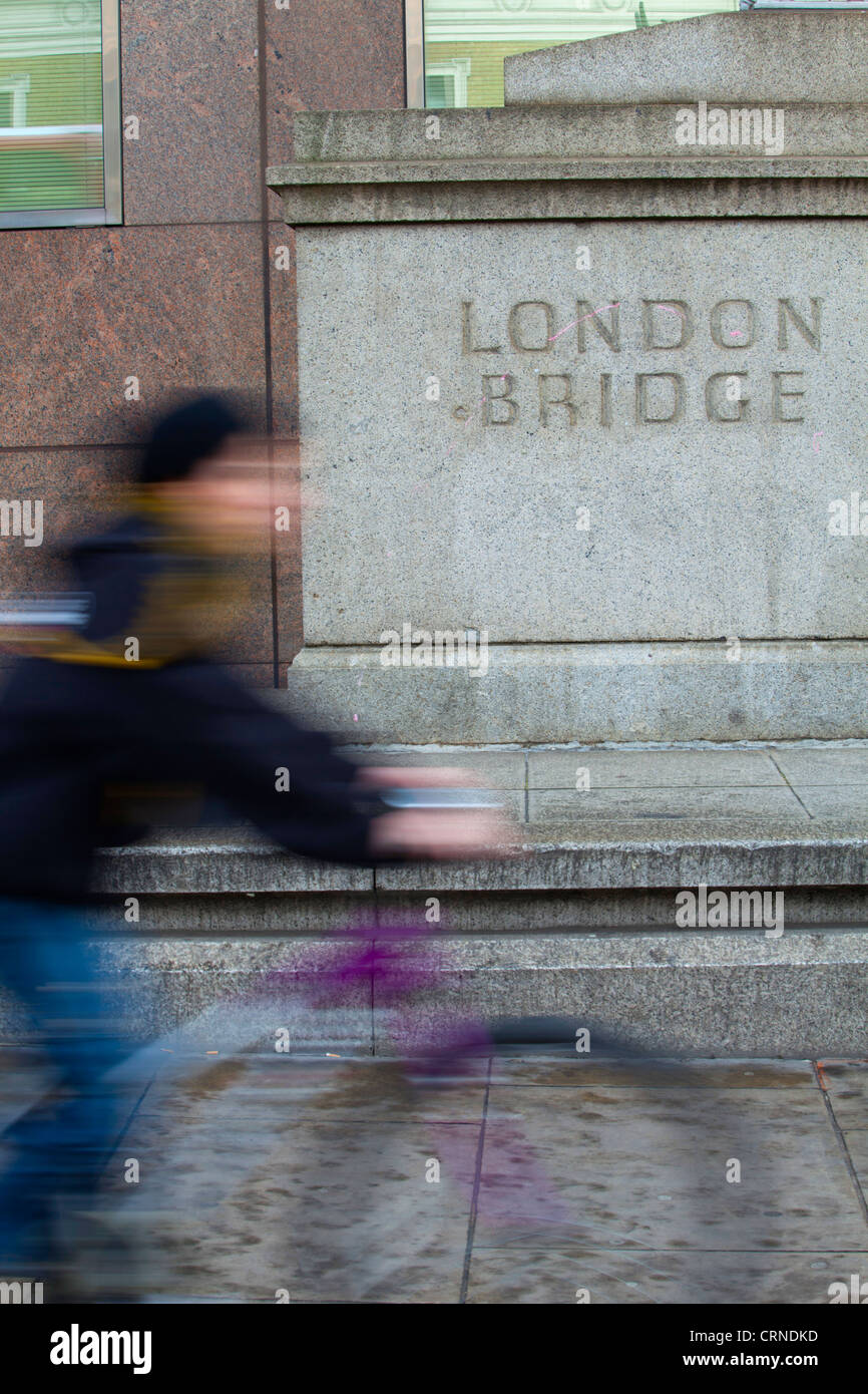 Los ciclistas que van más allá de un zócalo de piedra con el Puente de Londres talladas en ella. Foto de stock