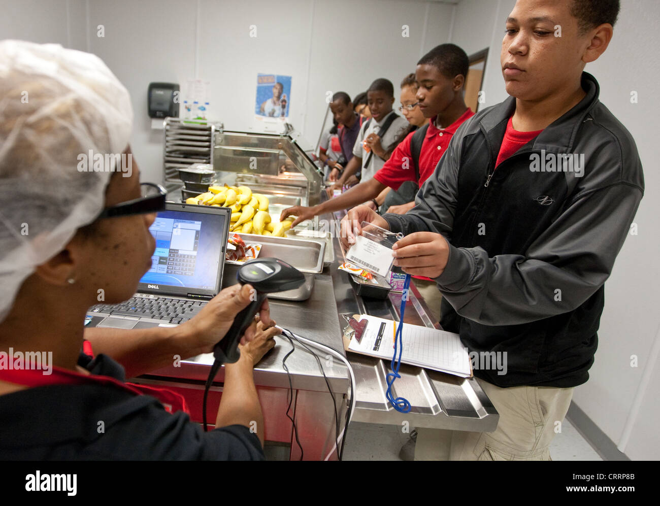 Cafetería trabajador utiliza el escáner de mano portátil para leer el código de barras la información sobre los estudiantes tarjetas de almuerzo escolar en carta pública high school Foto de stock