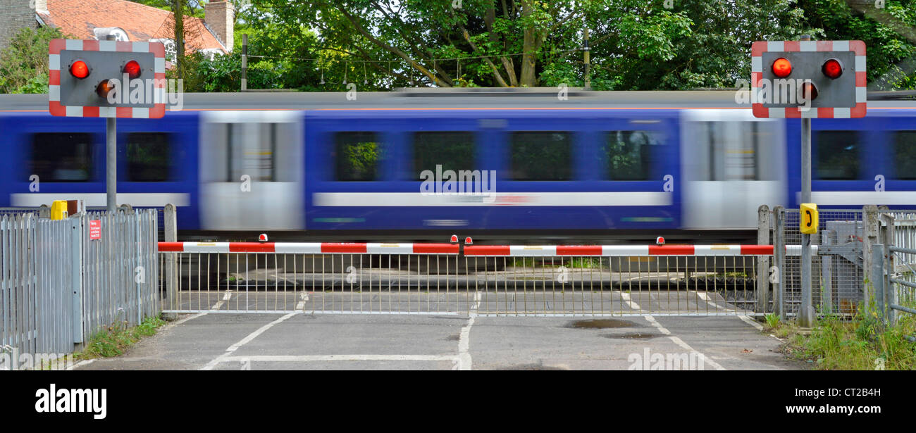 Las vías ferroviarias rojo parpadea la luz de advertencia de nivel de señal cruzar la barrera puertas country road tren de pasajeros en el desenfoque de movimiento Margaretting Essex, Inglaterra Foto de stock