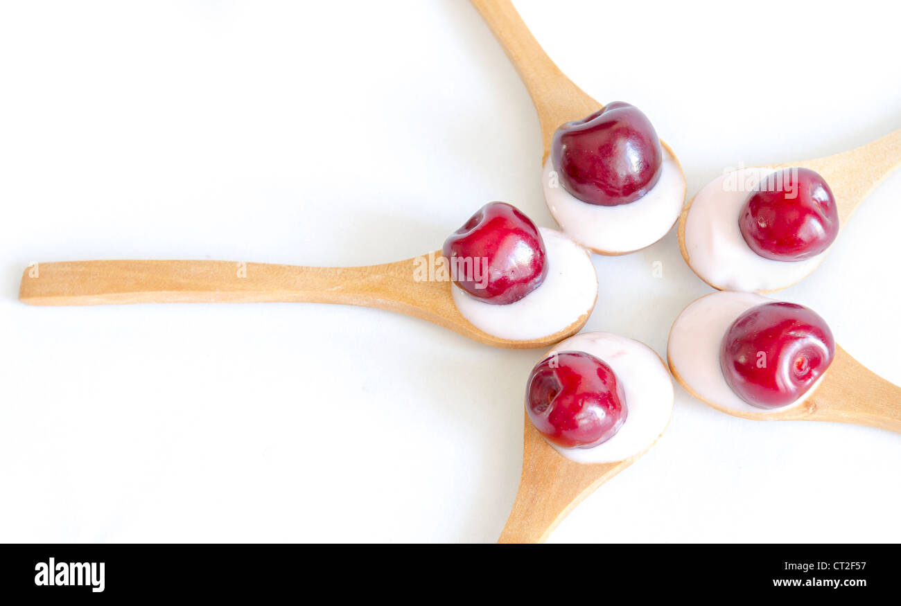 Cuchara de madera es con yogurt y las cerezas frescas sobre fondo blanco. Foto de stock
