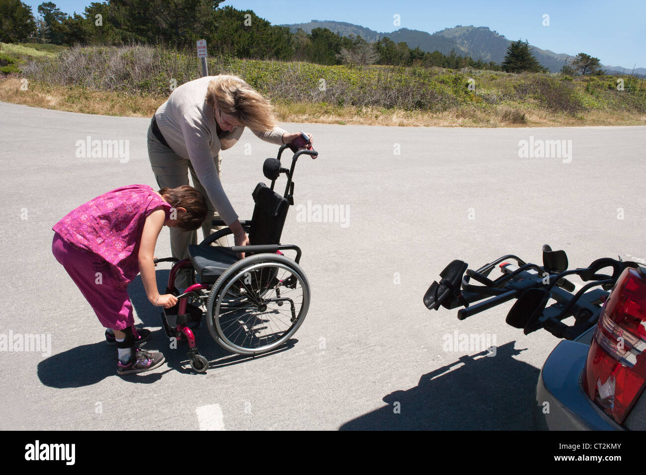 La madre y la hija de siete años ajustar la silla de ruedas para niño con distrofia muscular antes de ir de excursión en el norte de California, Estados Unidos. Foto de stock