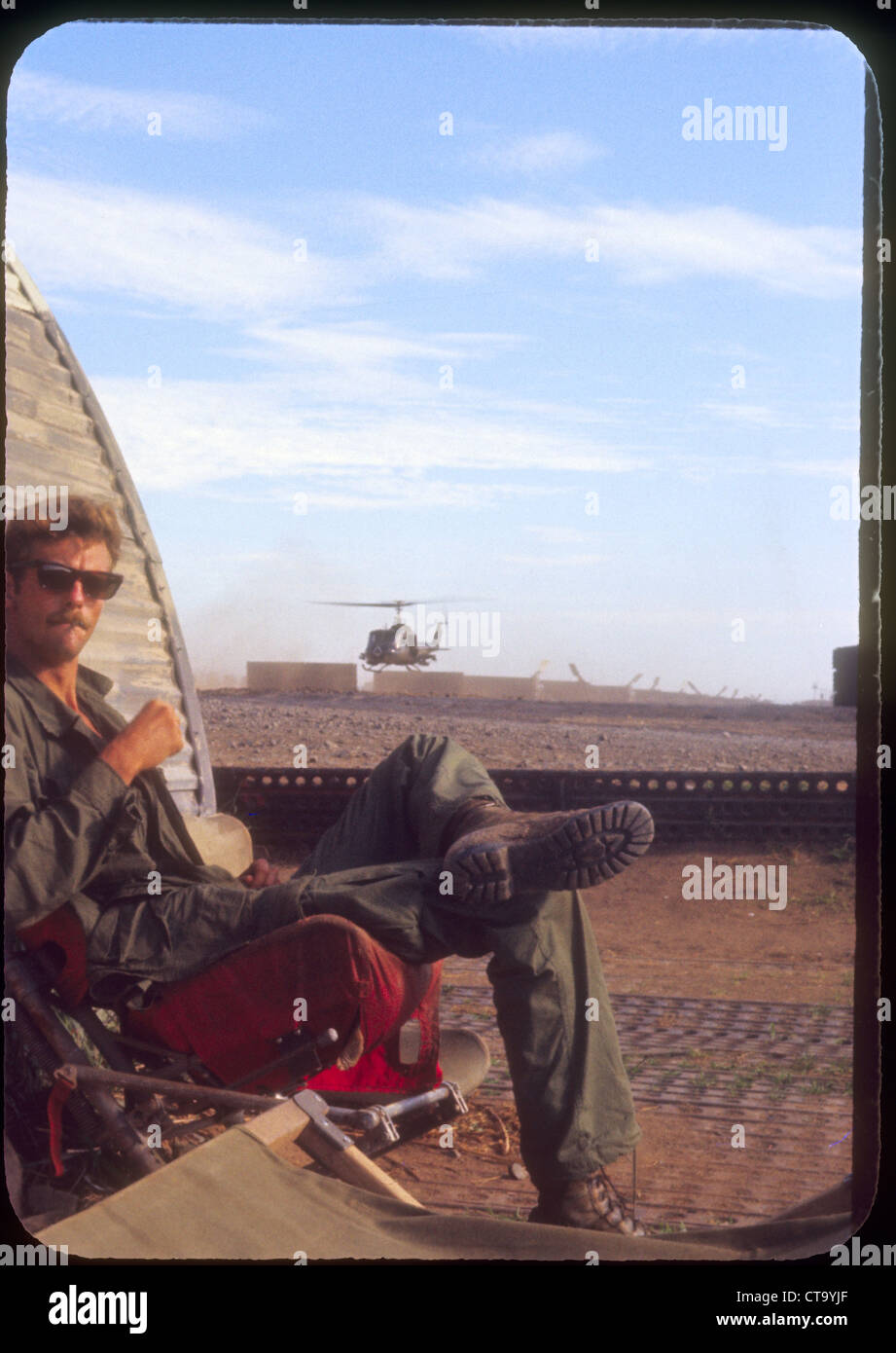 Soldado americano sentado junto a la línea de vuelo fortificaciones mientras huey helicóptero despega durante la guerra Vientnam Foto de stock