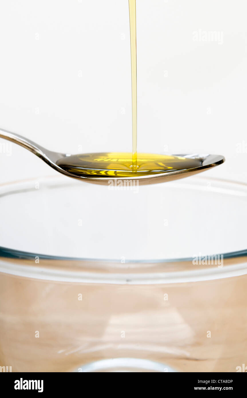 Se vierte el aceite de oliva en una cuchara en el tazón de vidrio. Foto de stock