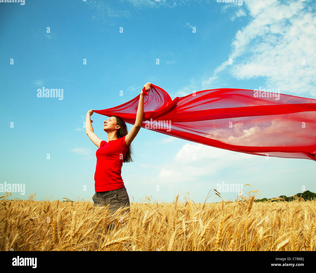 Jovencita en un campo de trigo con tela roja Foto de stock