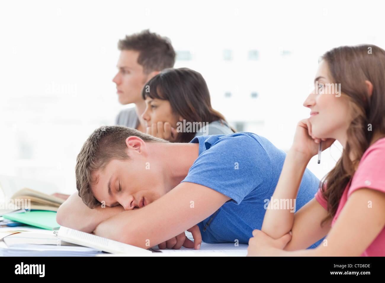 Cuatro estudiantes en clase como tres preste atención un estudiante varón duerme Foto de stock