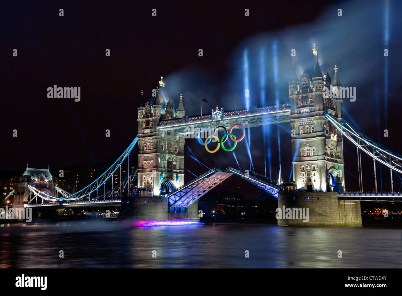 Un castillo de fuegos artificiales sobre el Tower Bridge, como la llama olímpica viaja bajo el puente hacia el estadio olímpico Foto de stock
