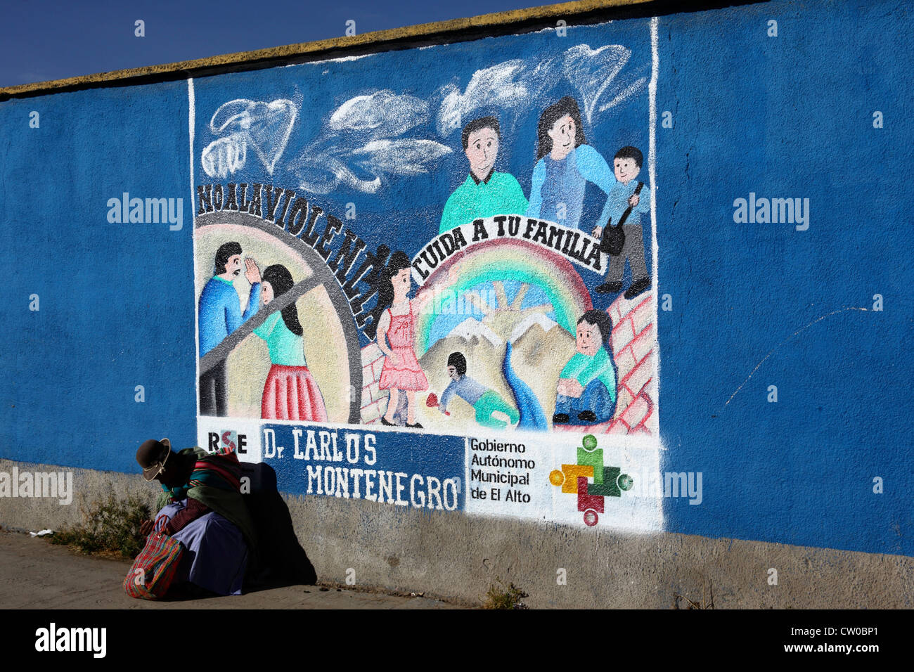 Mujer nativa sentada en el pavimento junto al mural que es parte de una campaña para reducir el abuso doméstico y la violencia contra las mujeres, El Alto, Bolivia Foto de stock