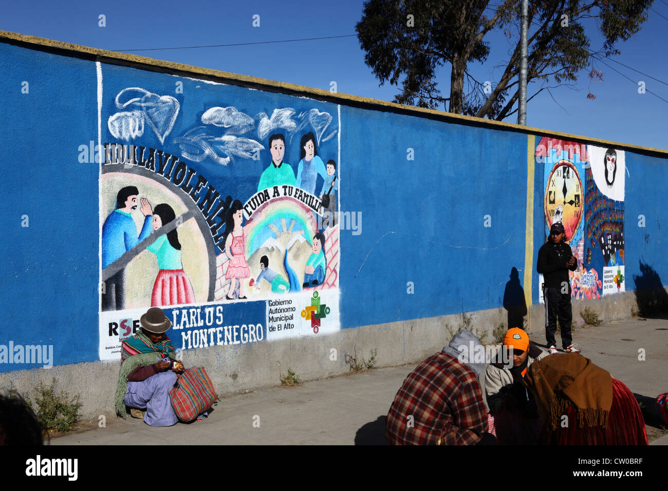 Mujer nativa sentada en el pavimento junto al mural que es parte de una campaña para reducir el abuso doméstico y la violencia contra las mujeres, El Alto, Bolivia Foto de stock