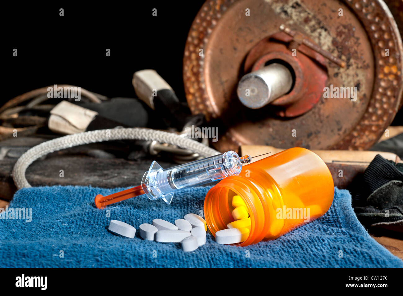 Medicamentos esteroideos incluyendo pastillas y una jeringa delante del equipo de ejercicio. Foto de stock