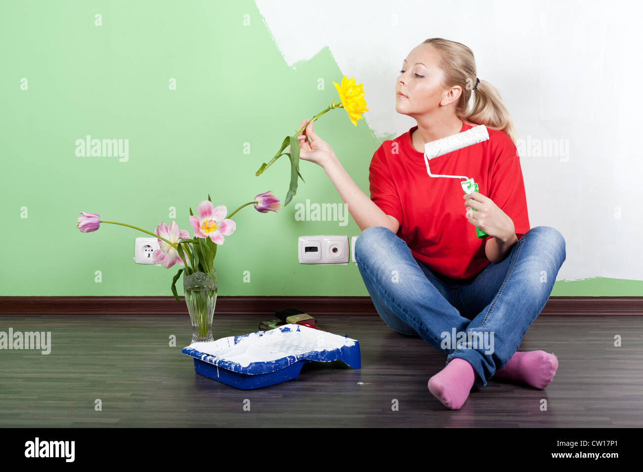 Mujer joven con flor y rodillo de pintura en manos de pintura de pared interior Foto de stock