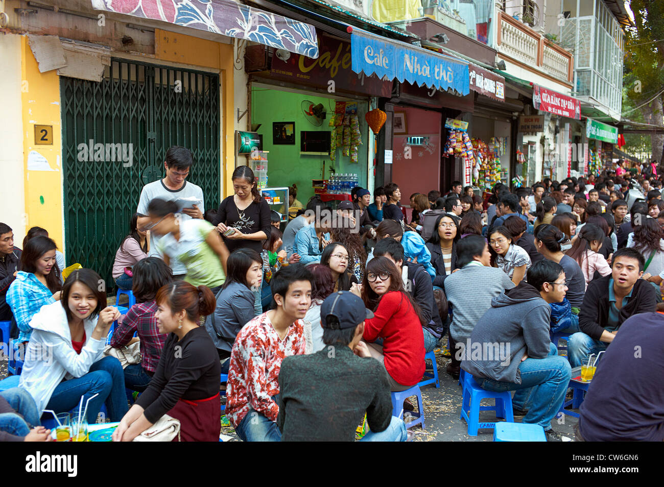 Una multitud de gente sentada en la calle delante de un café al aire libre con la antigua catedral de San José en el fondo. Foto de stock