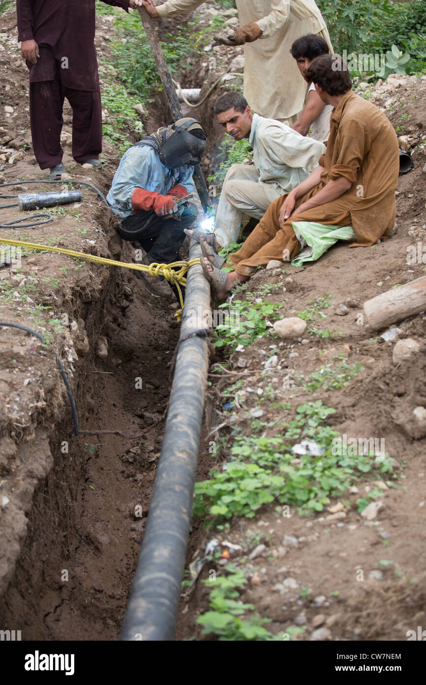 Hombre de soldar una tubería subterránea en dicho pueblo Pur, Islamabad, Pakistán Foto de stock