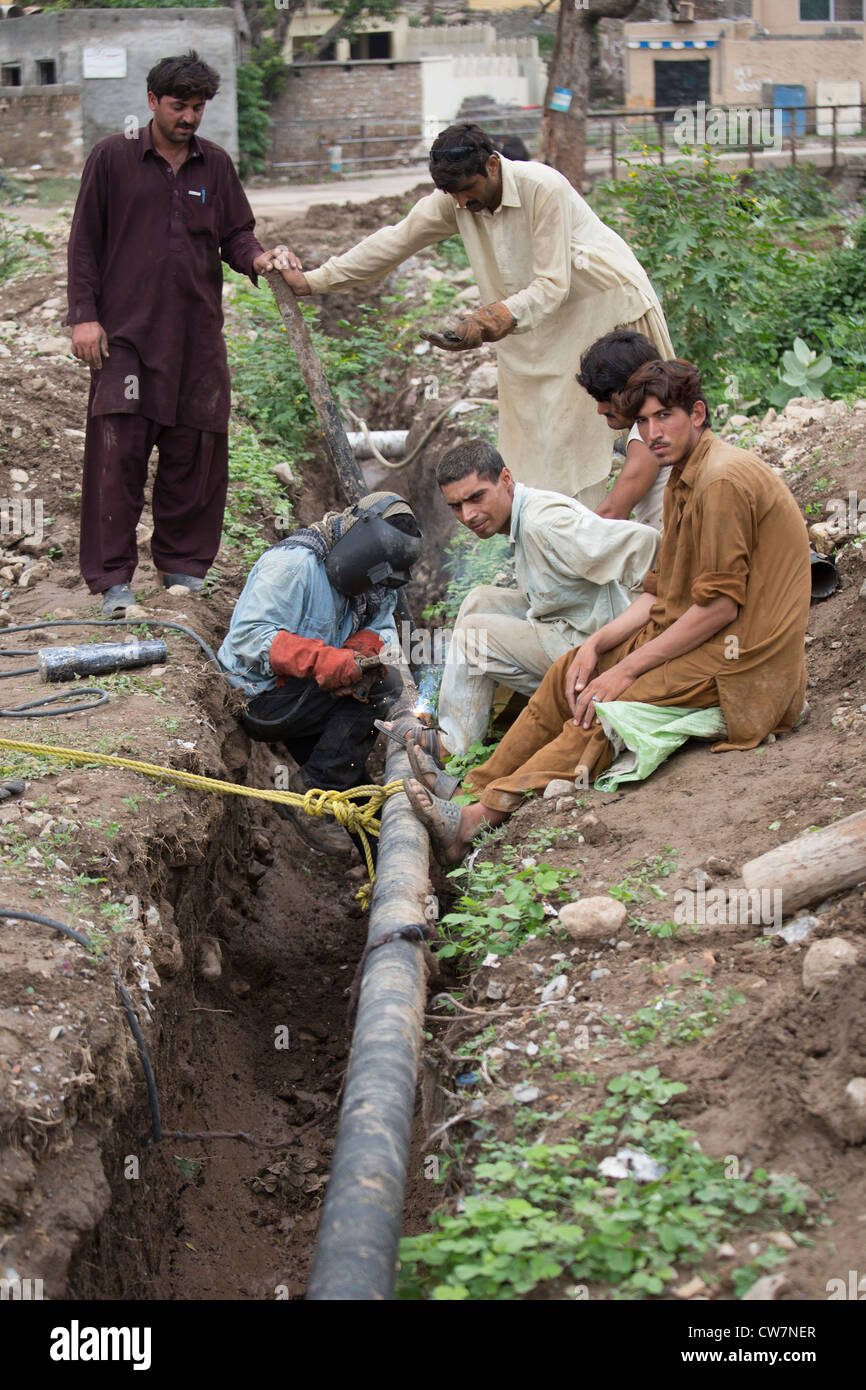 Hombre de soldar una tubería subterránea en dicho pueblo Pur, Islamabad, Pakistán Foto de stock