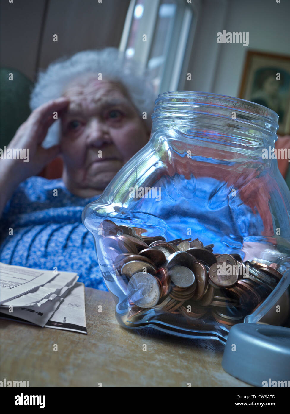 Problemas de dinero ancianos anciana anciana dama aprensivo con preocupaciones financieras vulnerables, en su sala de estar con bote de ahorro y papeles sobre la mesa Foto de stock