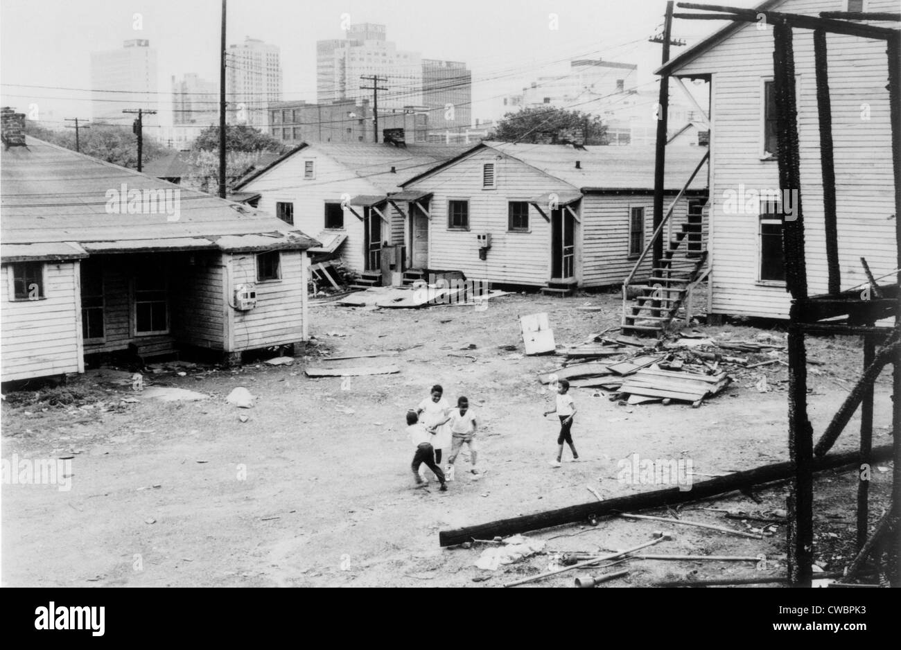 Niños africano-americanos jugando en tugurios en vista de edificios altos en segundo plano. Carolina del Norte, ca. 1966. Foto de stock