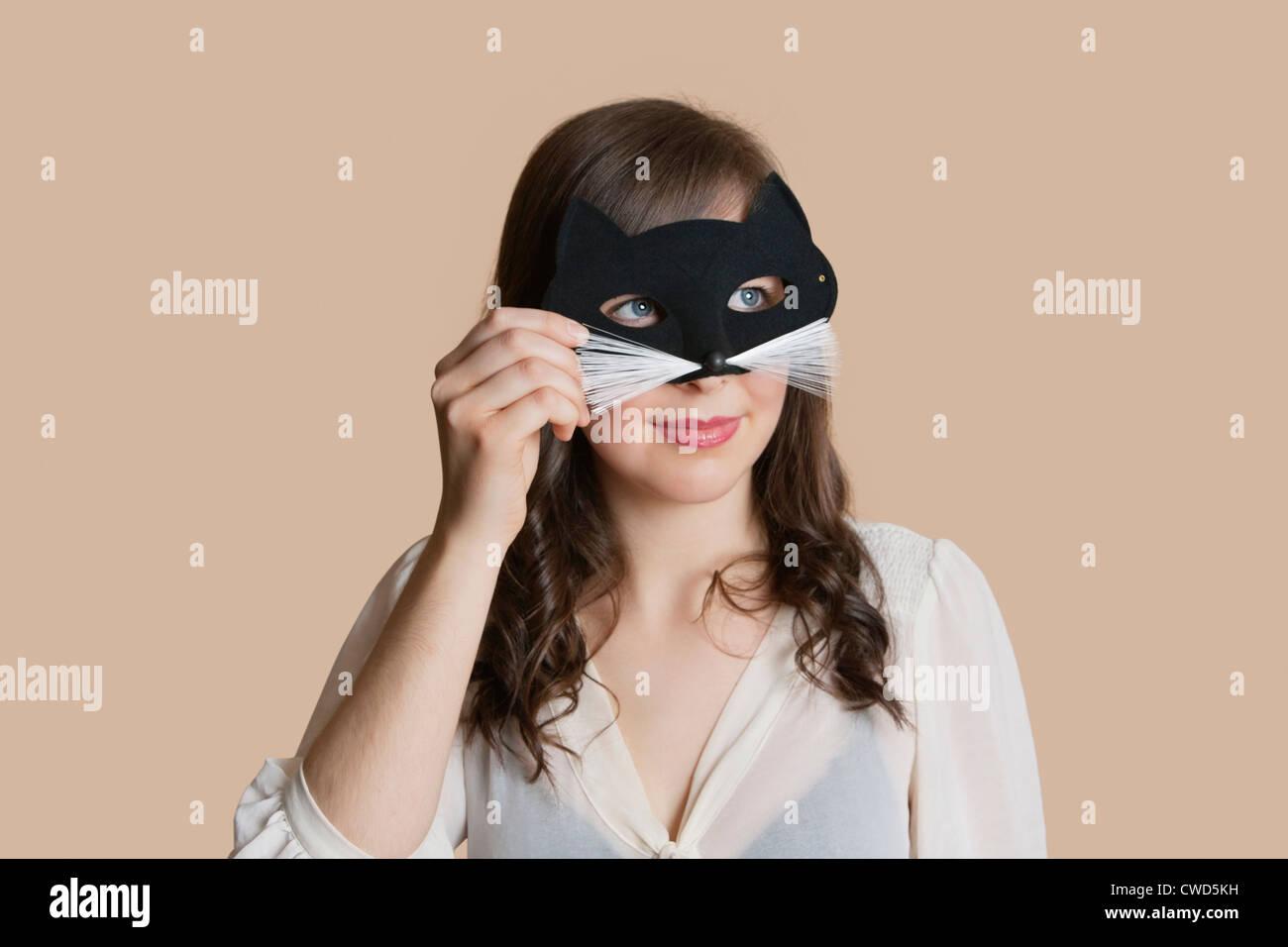 Mujer joven mirando a través del ojo máscara sobre fondo de color Foto de stock