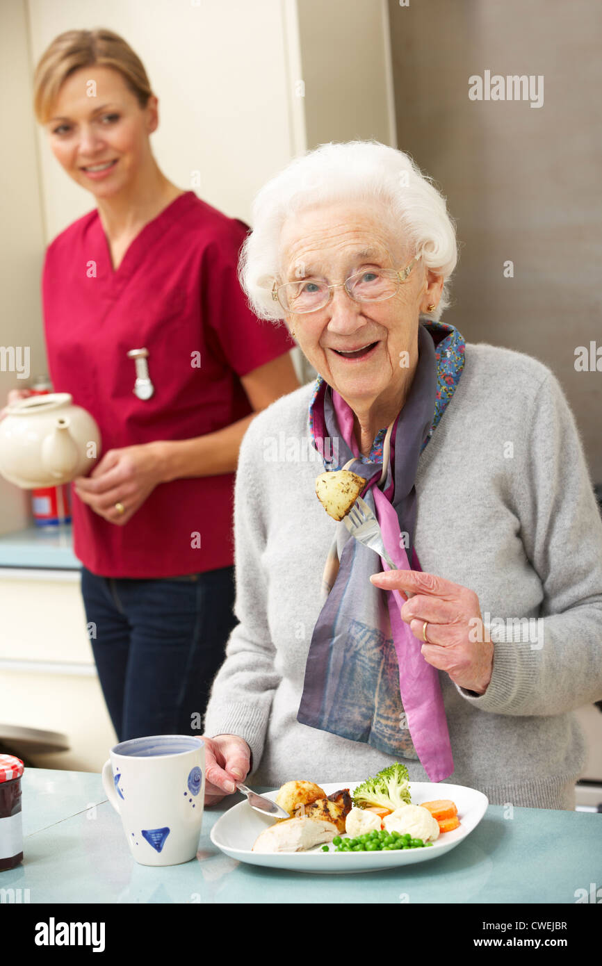 Mujer de más edad con cuidador comiendo comida en casa Foto de stock