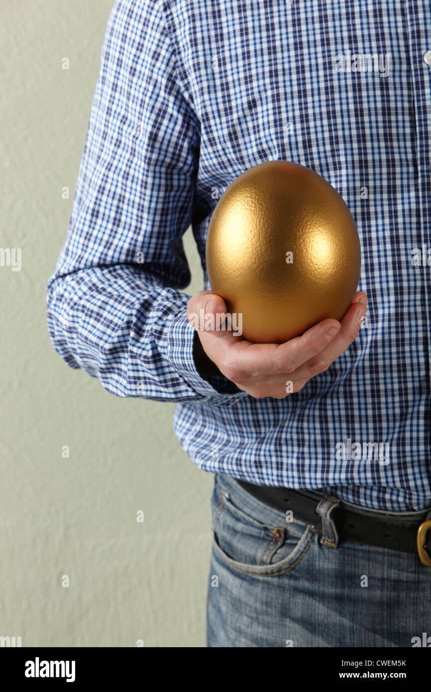 Foto de Estudio recortada del Hombre sujetando huevo de oro Foto de stock