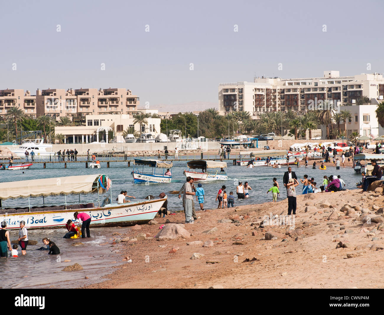 La playa pública en Aqaba, Jordania con los lugareños disfrutando el sol y  el agua. Se pueden alquilar barcos de cristal. El Mövenpick Hotel en  segundo plano Fotografía de stock - Alamy