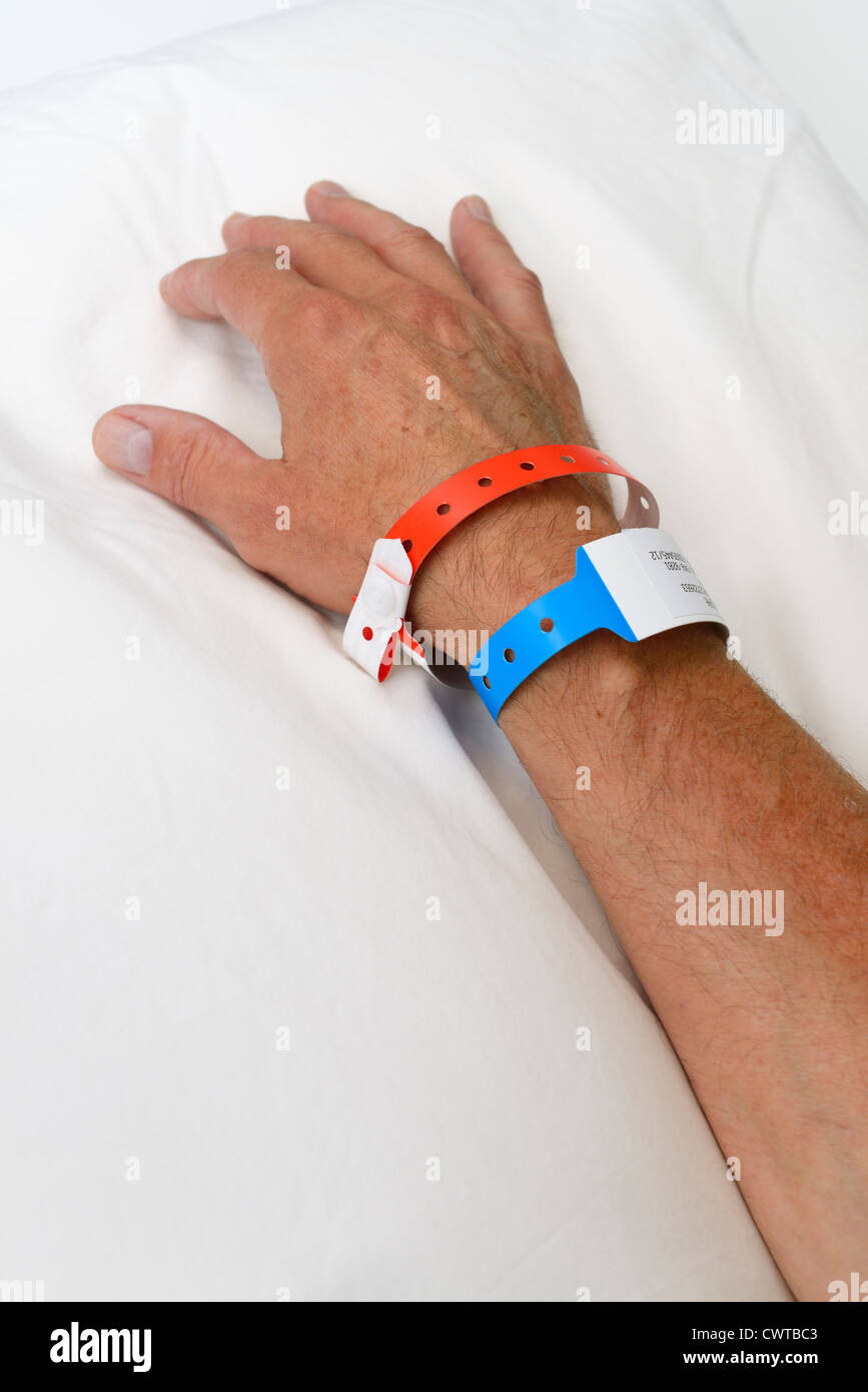 La mano y el brazo de un hombre en el hospital con muñequeras de identificación Foto de stock