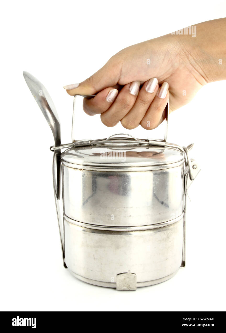 Una mano sujetando metal plateado tiffin y cuchara, contenedores de alimentos sobre fondo blanco. Foto de stock