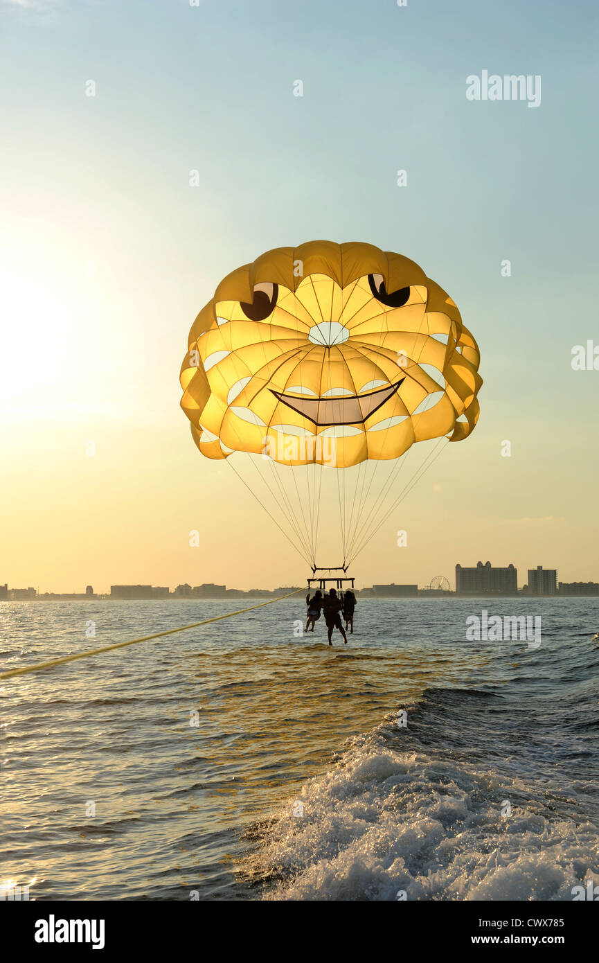Tres personas en un paracaídas en el océano durante una puesta de sol Foto de stock