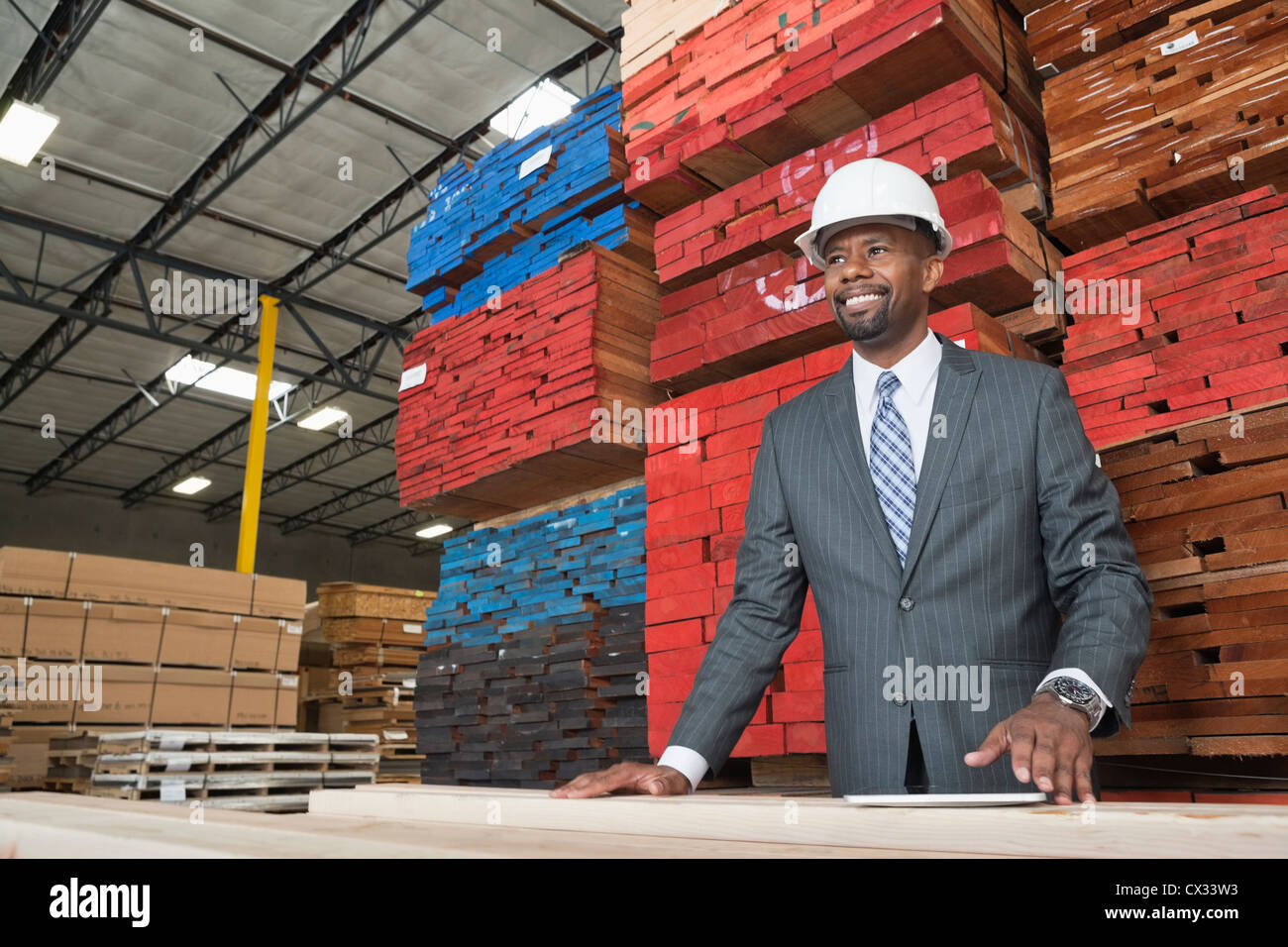 Un contratista de hombres afroamericanos de pie delante de tablones de madera apilada Foto de stock