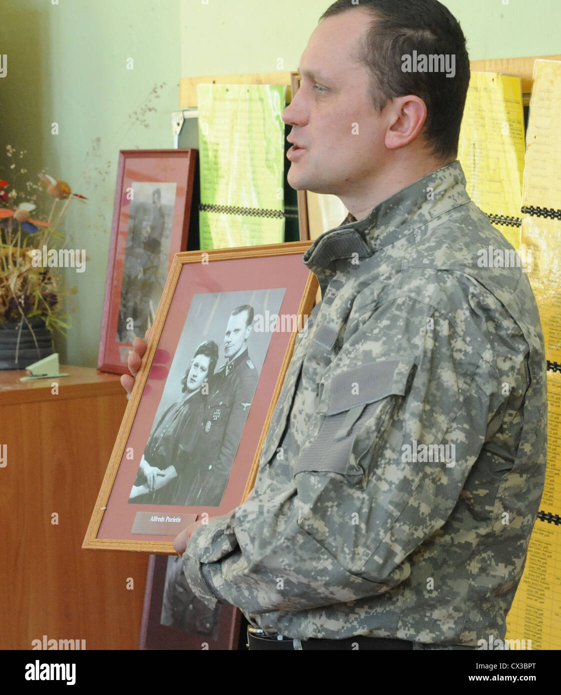 ITAR-TASS: Letonia. Marzo 11, 2012. Un hombre en uniforme de faena muestra  una fotografía de un miembro de la legión letona y un joven durante una  lección de \