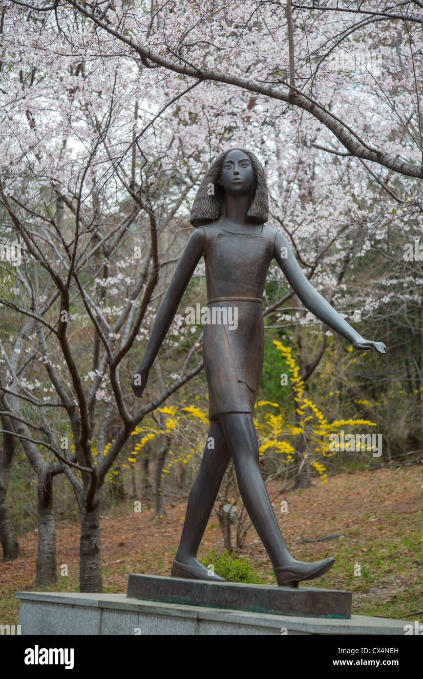 Estatua de bronce de una niña caminando delante de los cerezos en flor Jangbogsan montaña cerca Jinehae, Corea del Sur Foto de stock