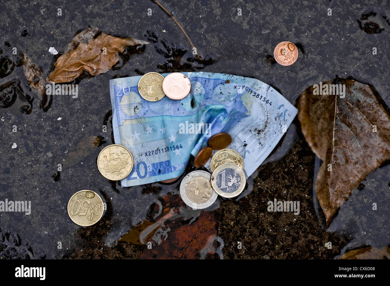 Una veintena de billetes y monedas en euros en un charco Foto de stock