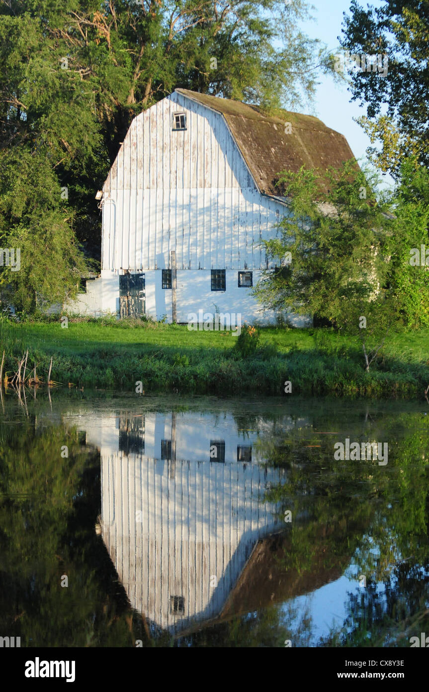 Hermoso blanco granero en el país con un reflejo en un estanque Foto de stock