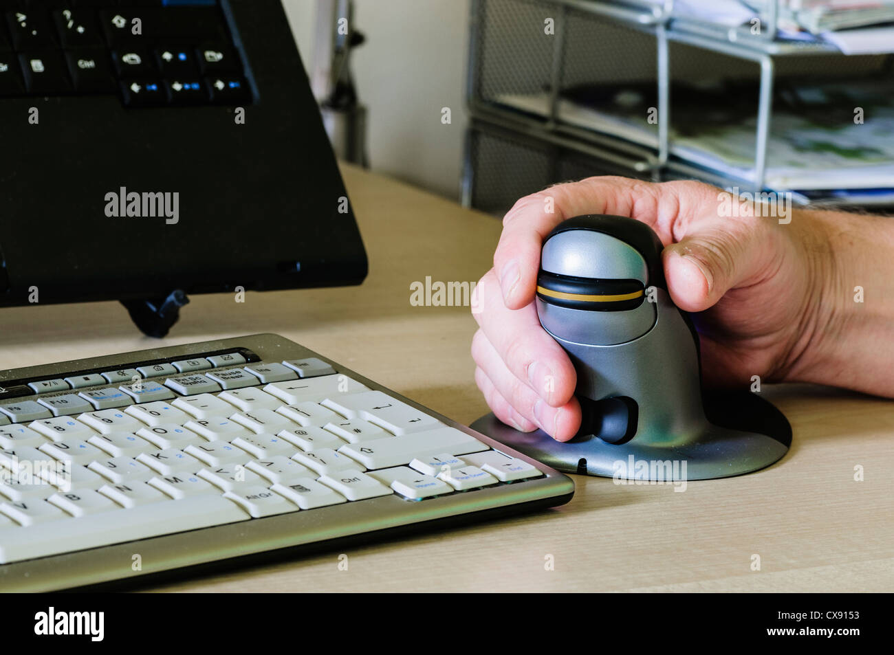 El hombre utiliza un pingüino vertical del ratón del ordenador ergonómico para personas con dolor de muñeca Foto de stock