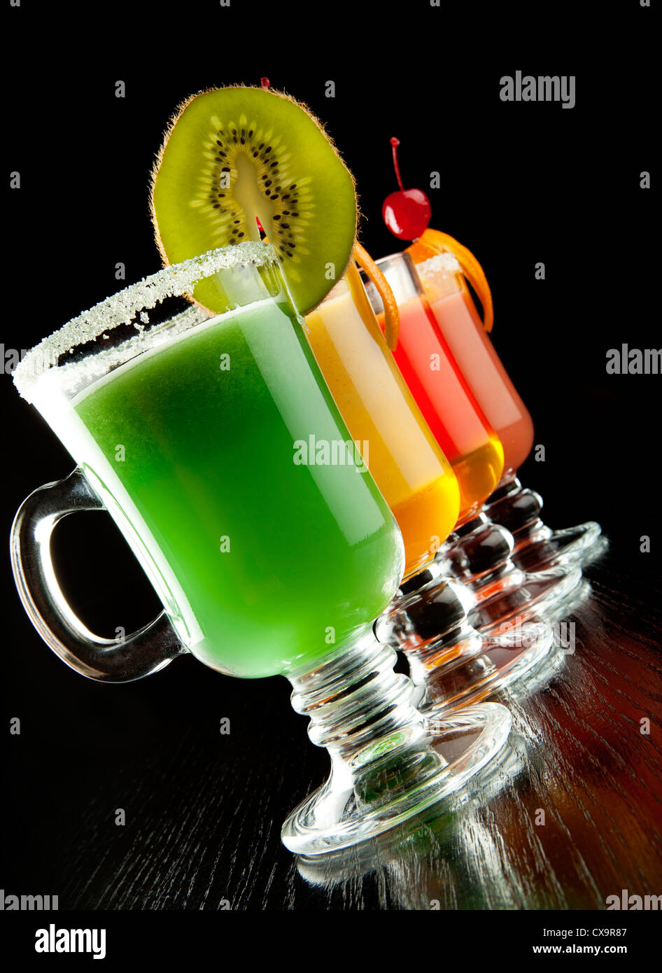 El grupo de cuatro copas de vino con coloridas bebidas cócteles, decorados con frutas y azúcar negra sobre el mostrador de bar Foto de stock