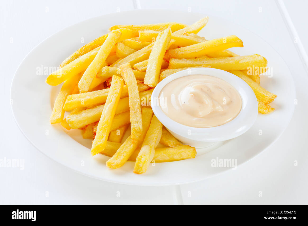 Un plato de patatas fritas con mayonesa en un pequeño recipiente. Foto de stock