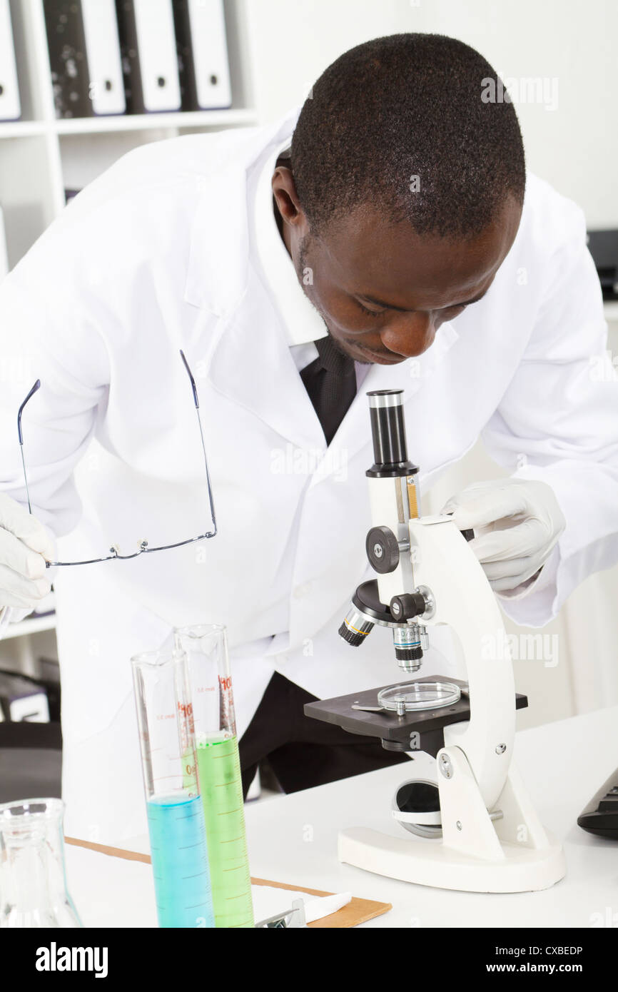 Macho americano africano investigador del laboratorio mirando a través del microscopio Foto de stock