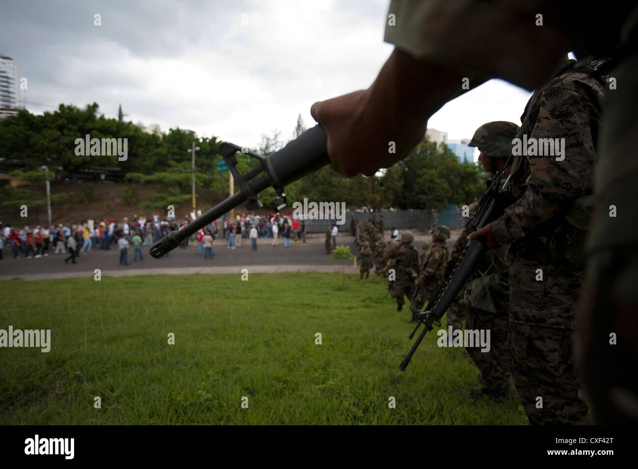 Soldados hondureños montan guardia como simpatizantes del depuesto presidente de Honduras, Manuel Zelaya, pasar por durante una marcha Foto de stock