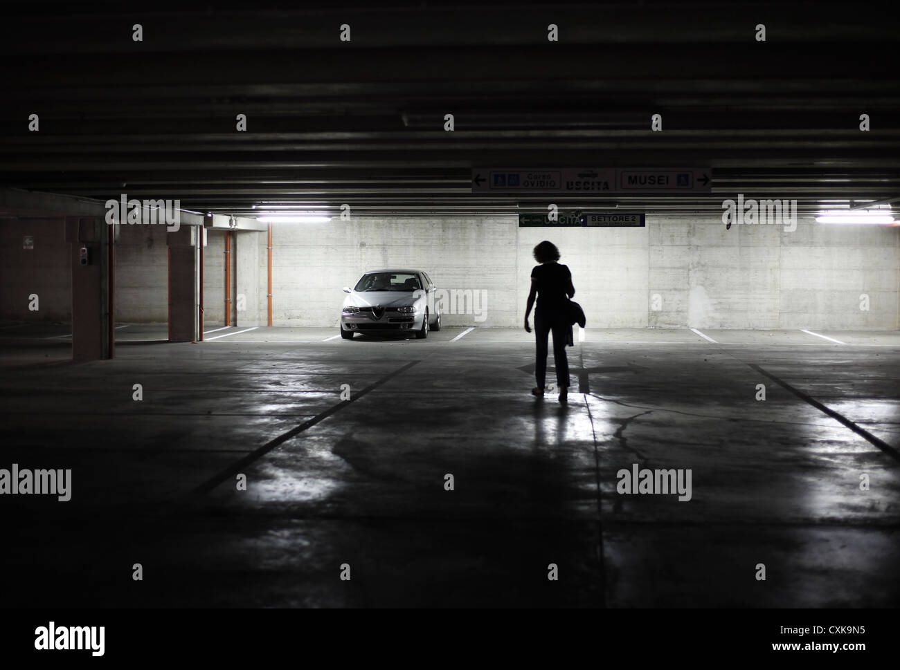 Una solitaria mujer regresa a su coche en un aparcamiento subterráneo solitaria. Foto de stock