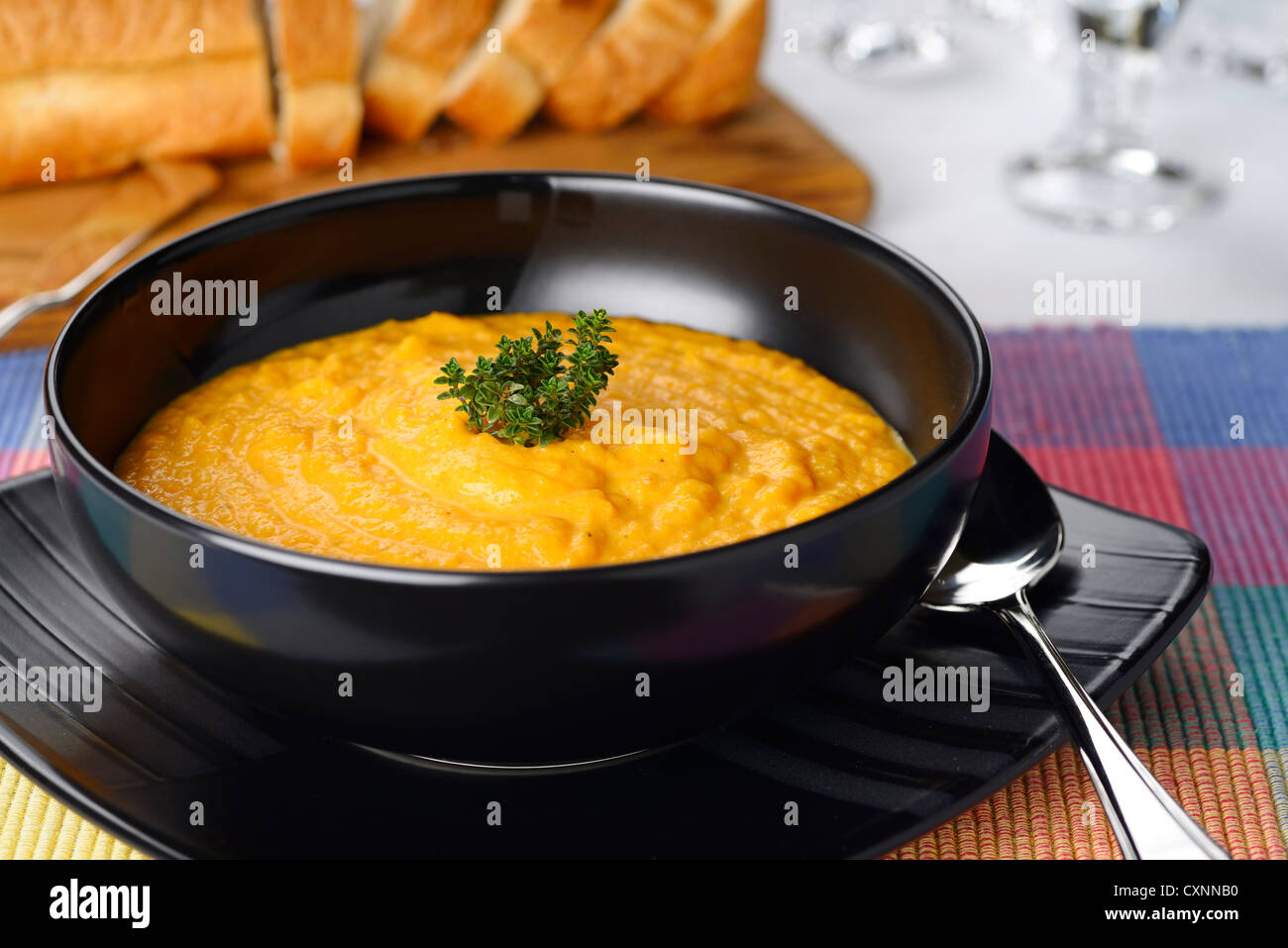 Crema de tomate zanahoria naranja sopa con tomillo aderezo en negro bowl con rebanadas de pan Foto de stock