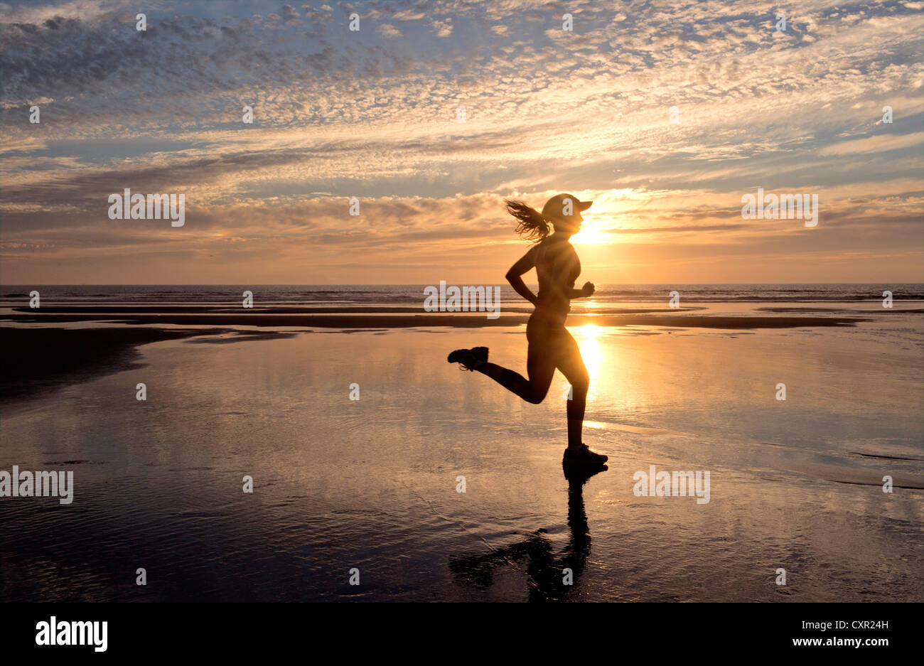 Mujer corriendo en la playa al amanecer. Foto de stock
