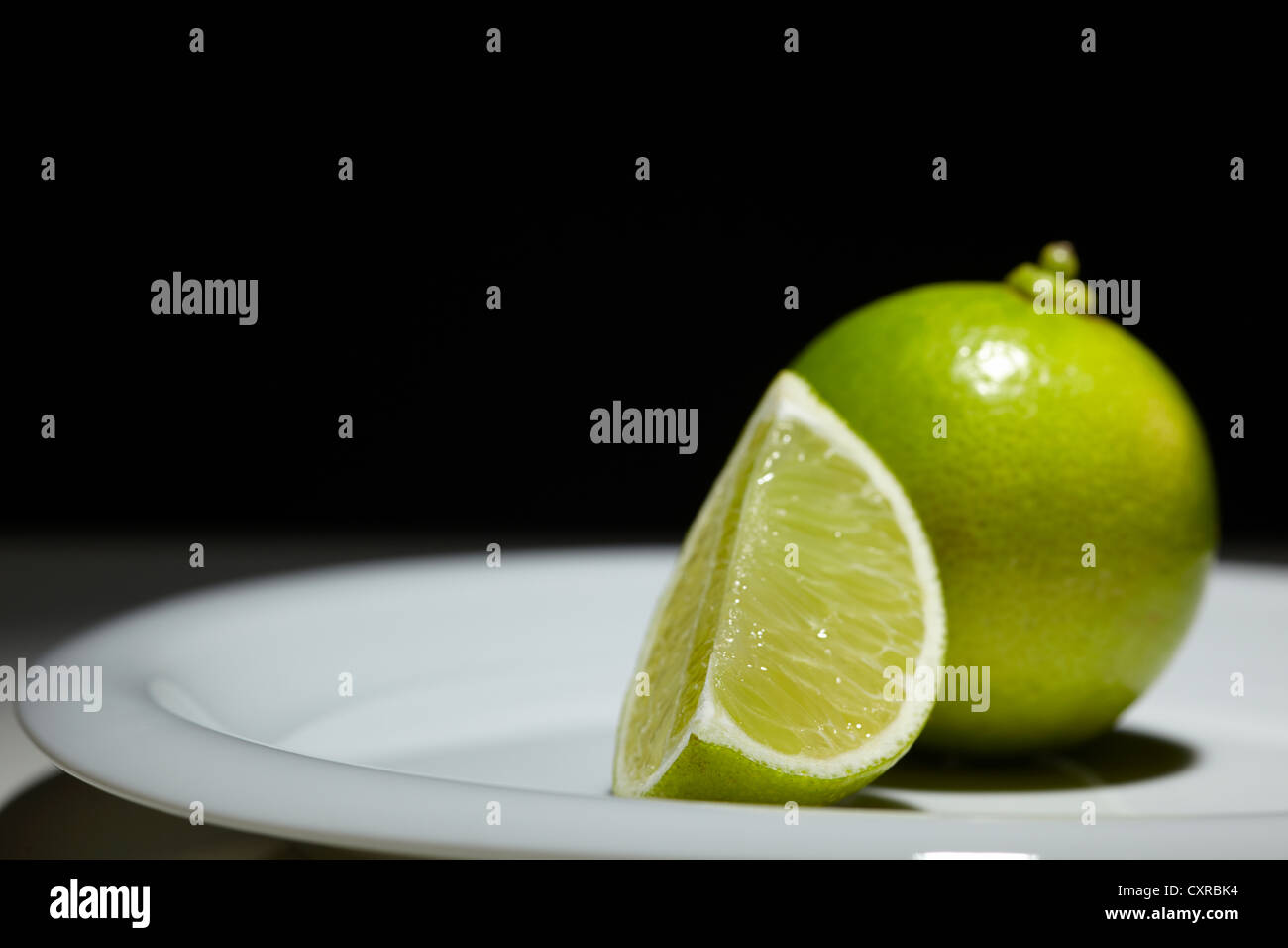 Limón (Citrus latifolia), enteras o en rodajas, sobre una placa blanca. Foto de stock