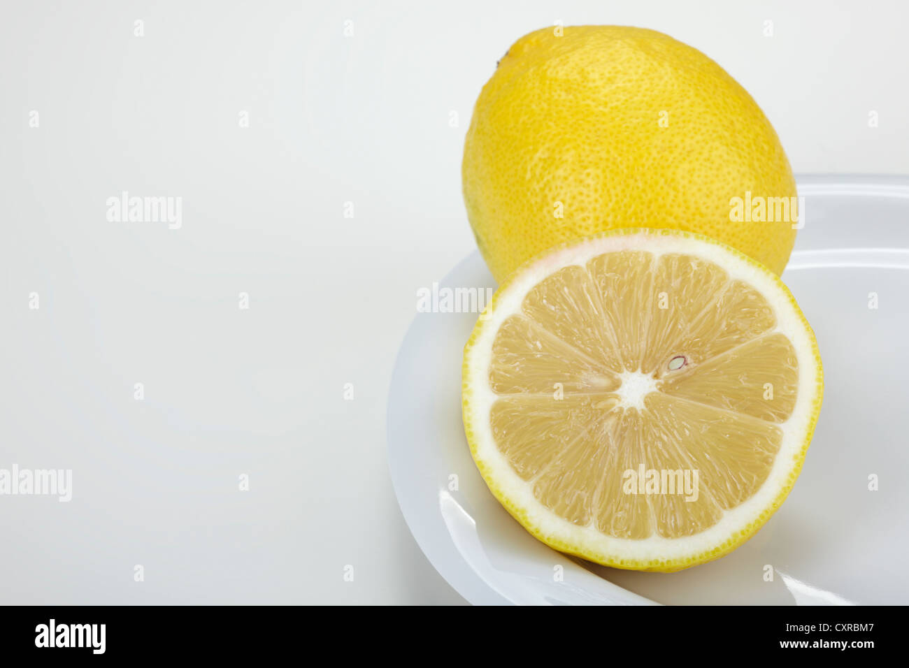 Limón (Citrus limon), enteras y cortadas por la mitad, sobre una placa blanca. Foto de stock