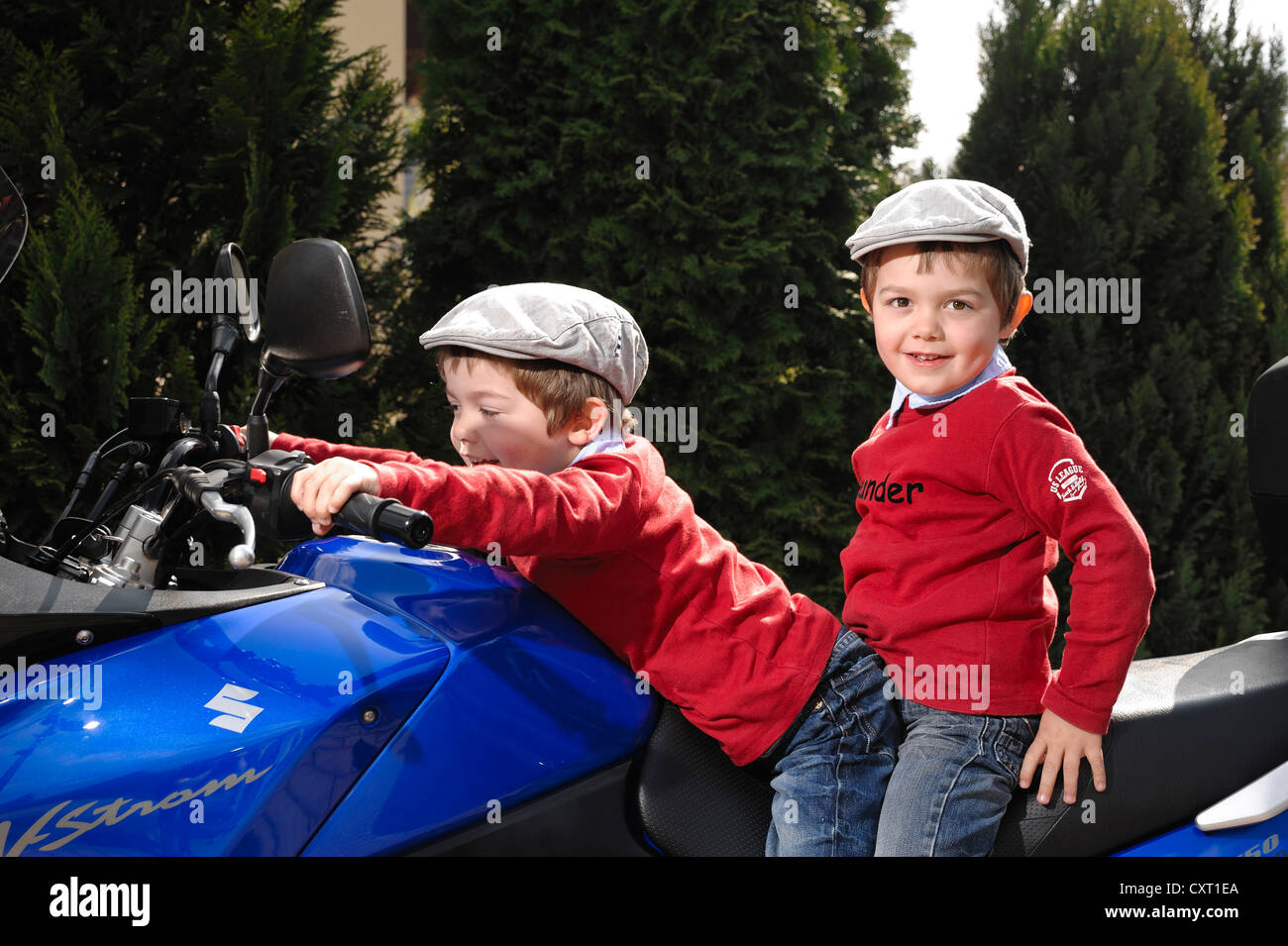 Gemelos, 4, usando tapones planos mientras están sentados juntos en una motocicleta azul Foto de stock