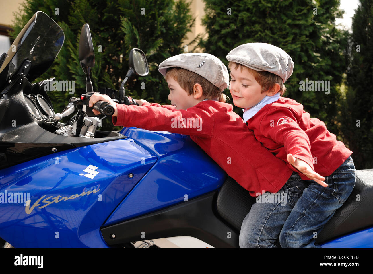 Gemelos, 4, usando tapones planos mientras están sentados juntos en una motocicleta azul Foto de stock