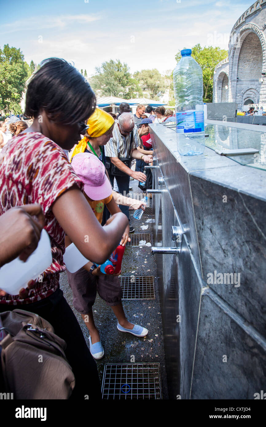 Los peregrinos llenando botellas con agua bendita en el Santuario de Lourdes, Hautes Pyrenees, Francia Foto de stock