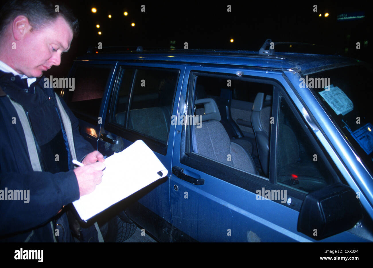 Un detective de policía escribe un informe acerca de la posición de los agujeros de bala en un coche después de un tiroteo de pandillas en Chicago, Estados Unidos. Foto de stock