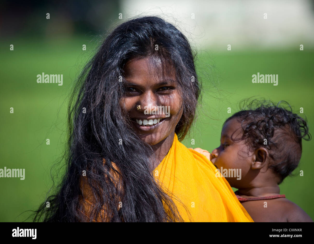 Sonriente joven madre con su largo cabello negro sostiene a su bebé en brazos, Periyar, India Foto de stock