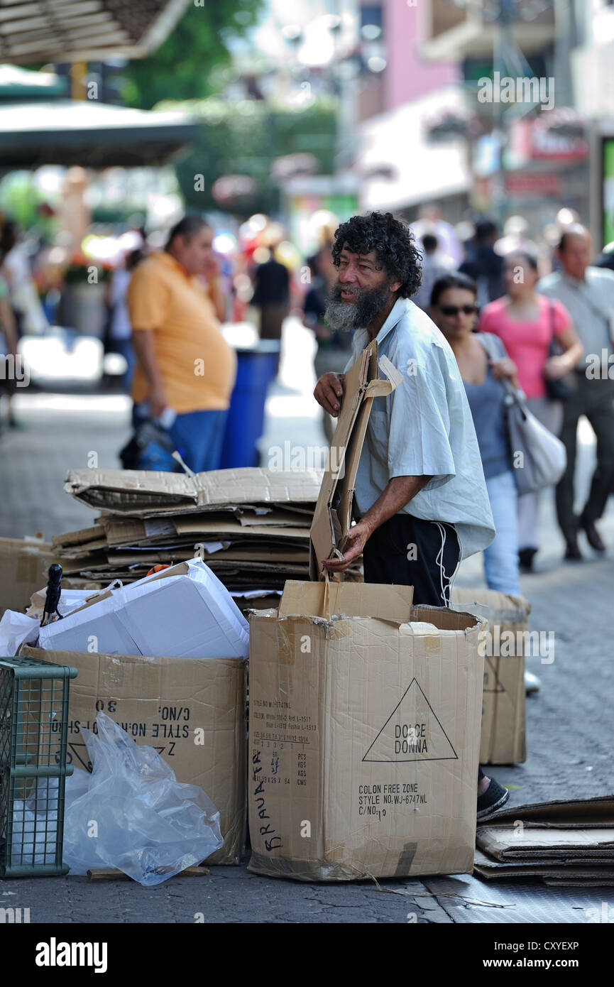 Pobre hombre ordenar productos reciclables o recursos, cajas de cartón fuera de una tienda, con el fin de venderlas a una planta de reciclaje Foto de stock