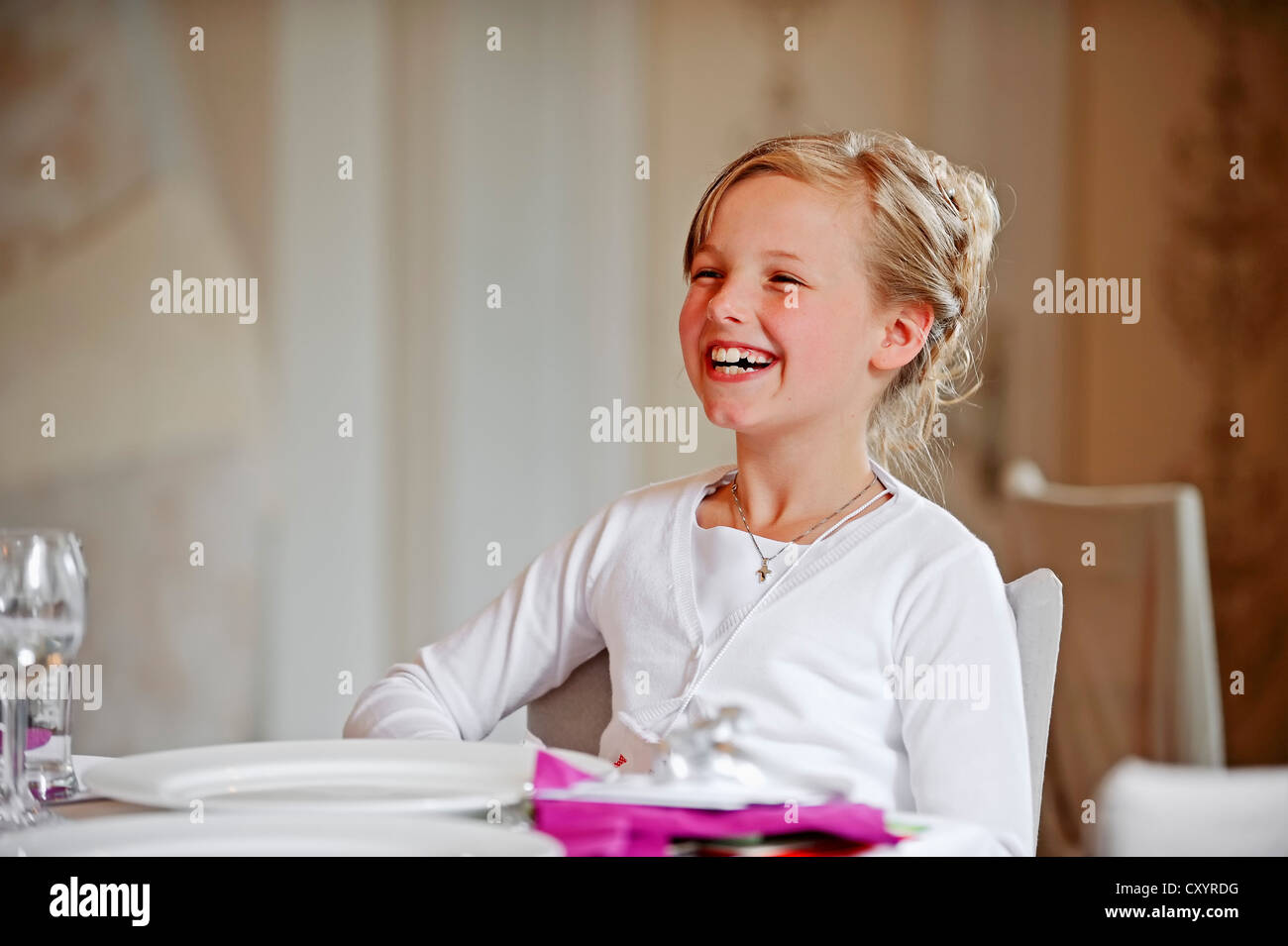 Niña de 9 años, sonríe a la mesa de la cena en el día de su Primera Comunión, región de Muensterland, Renania del Norte-Westfalia Foto de stock