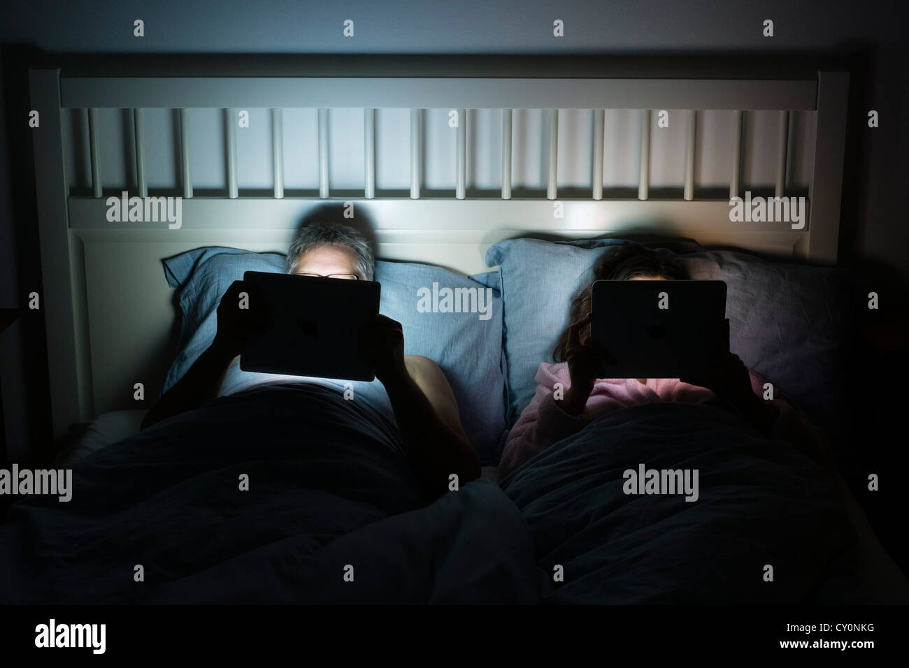La pareja en la cama en la noche, ambos usando iPad tablet pc Foto de stock
